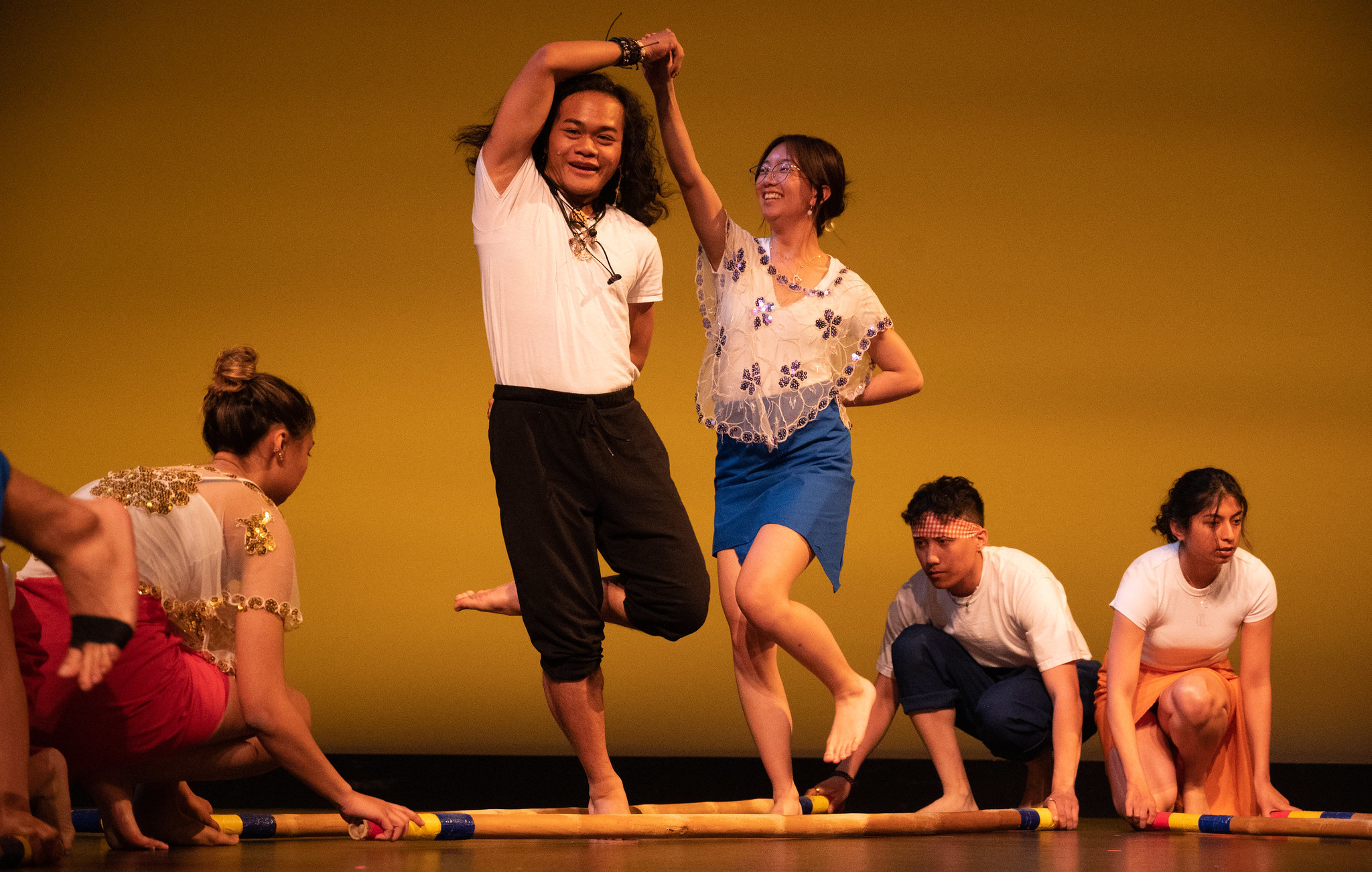 Two performers dancing between bamboo sticks.