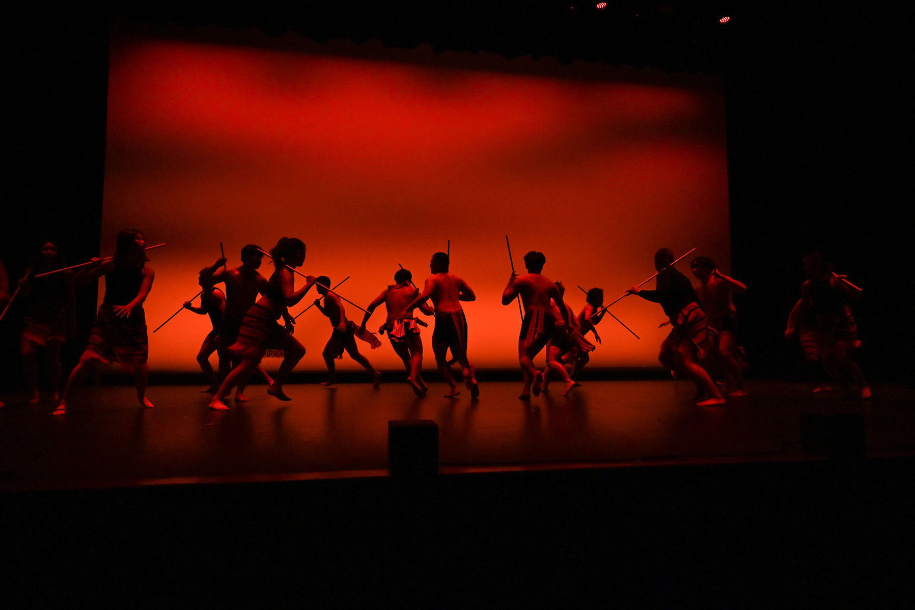 Group of dancers running around the stage in red lighting.